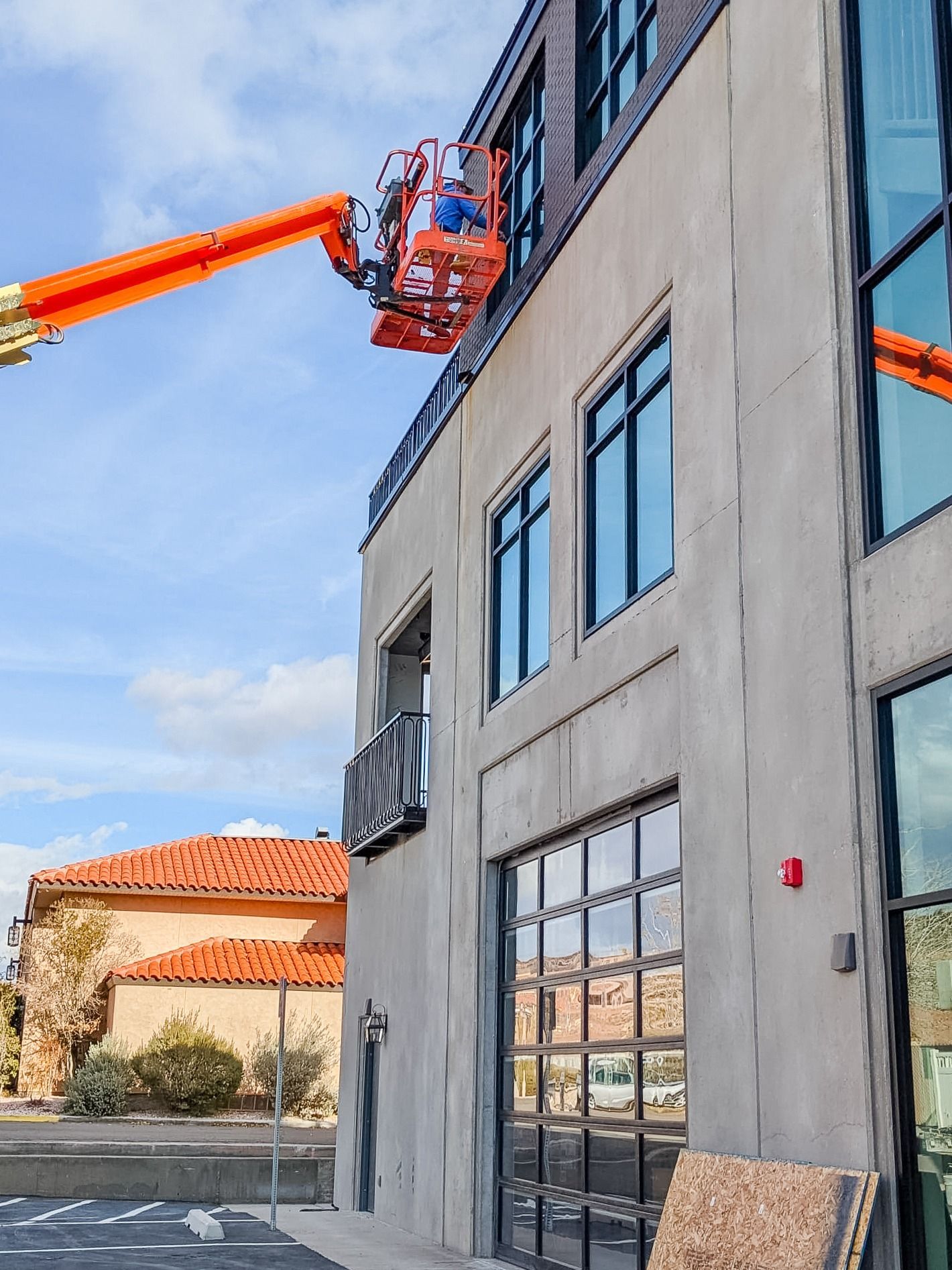 An orange boom lift with a worker in the basket reaches toward the windows of a multi-story concrete building.