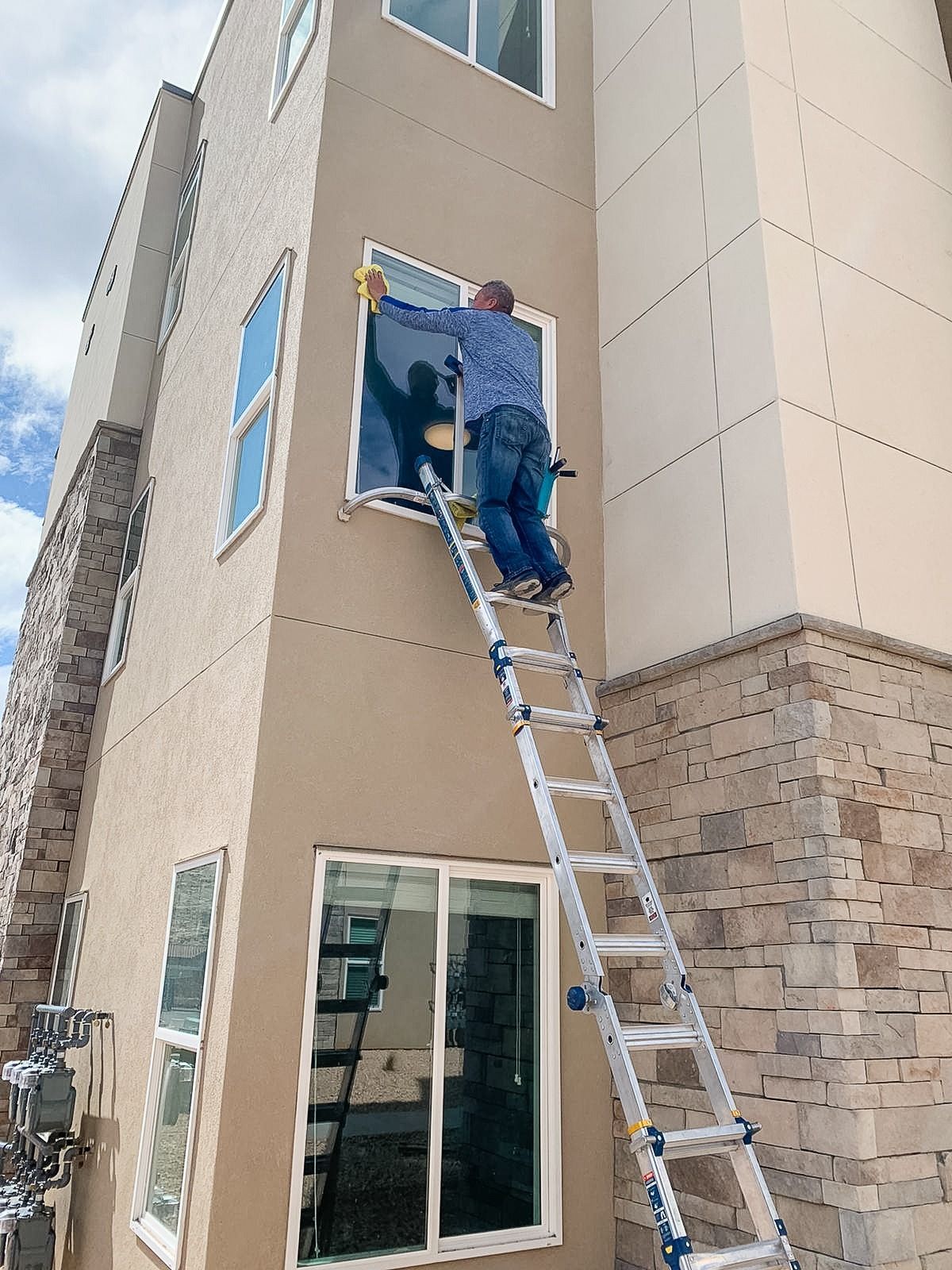 A person standing on an extended ladder outside a multi-story building, cleaning an upper-level window.