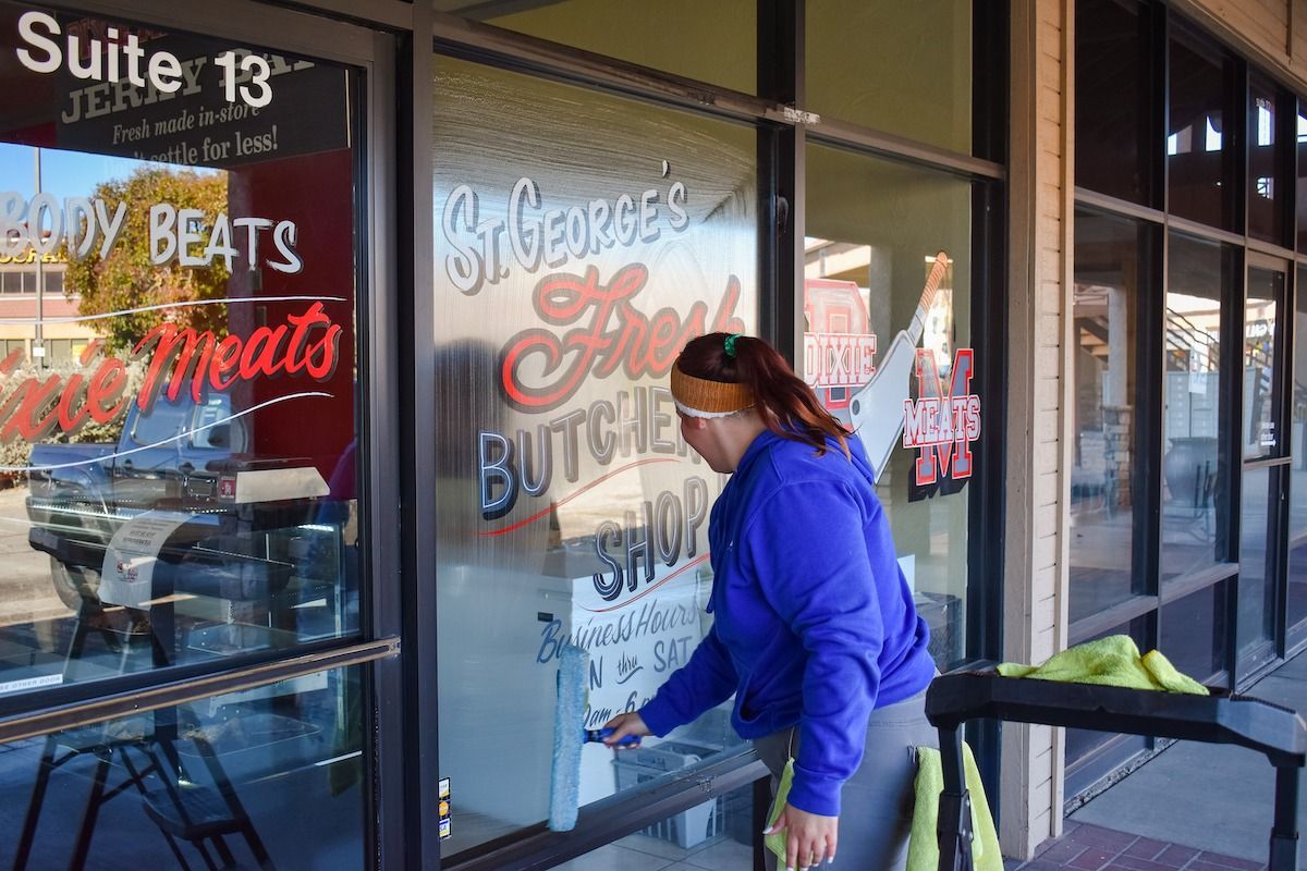 A person in a blue hoodie paints white lettering onto the glass storefront of 