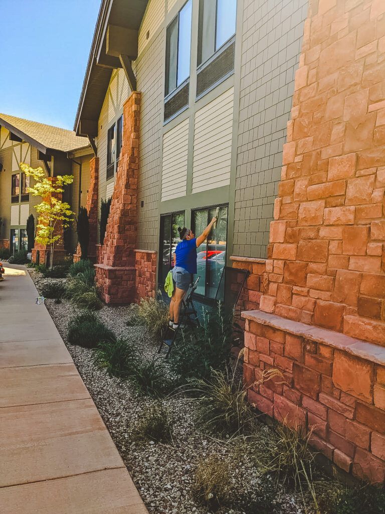 A person in a blue shirt cleans a window on the stone and siding exterior of a modern residential building.