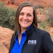 Smiling person wearing a blue polo and black jacket with a DSS logo, posed against a red rock desert background.