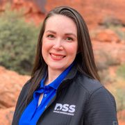 A woman smiles while wearing a blue polo shirt and black jacket with a