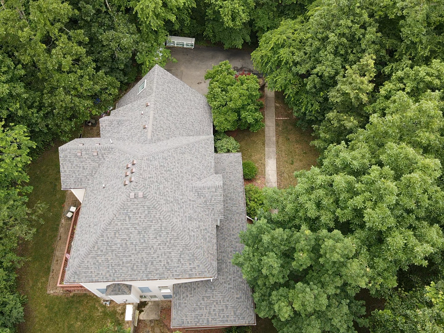 Aerial view of a gray-roofed house surrounded by green trees and a pathway leading to a driveway.
