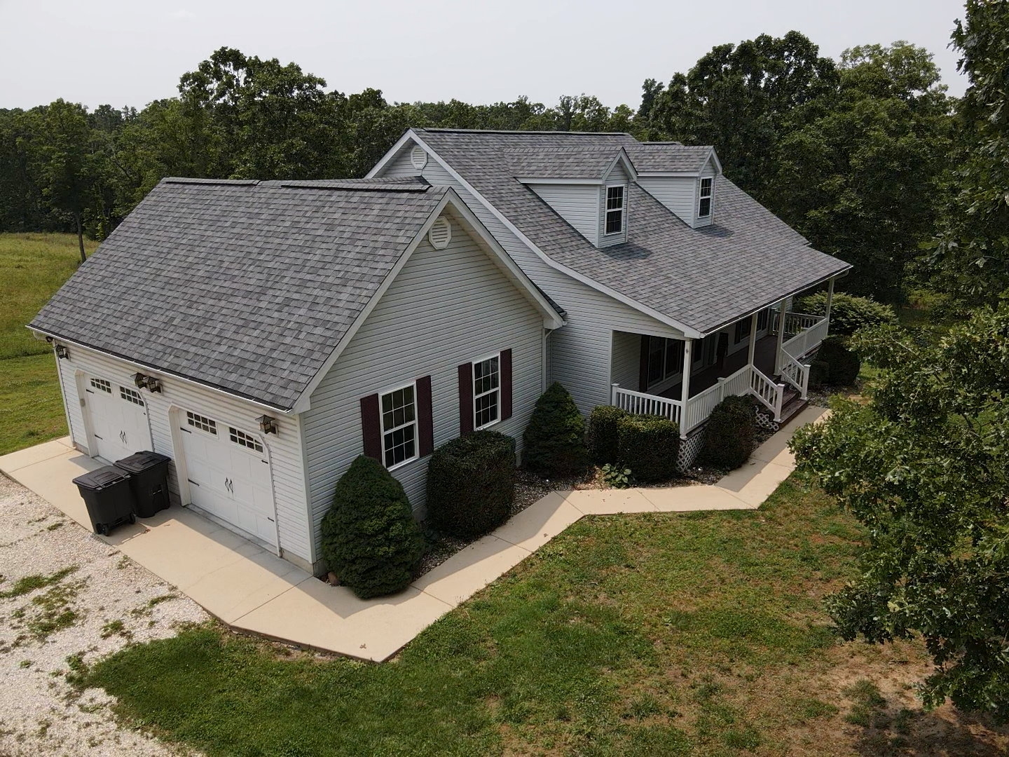 Gray house with attached garage, two dormers, and porch surrounded by trees.