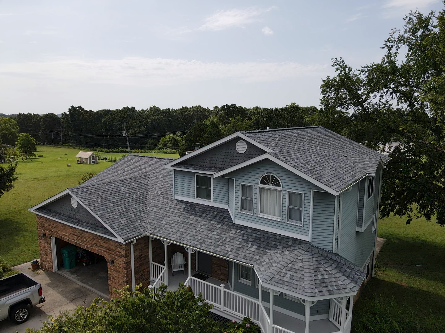 Blue two-story house with gray roof, brick accents, and a porch, with a truck parked in the driveway.