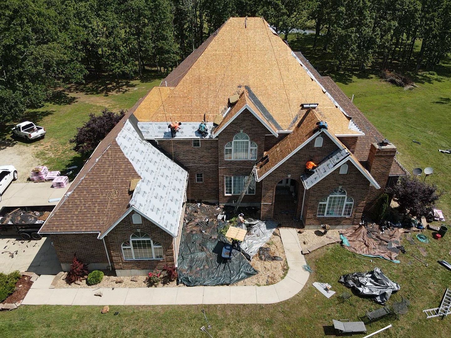 Roofers working on a residential home with new roofing installation, surrounded by green grass.