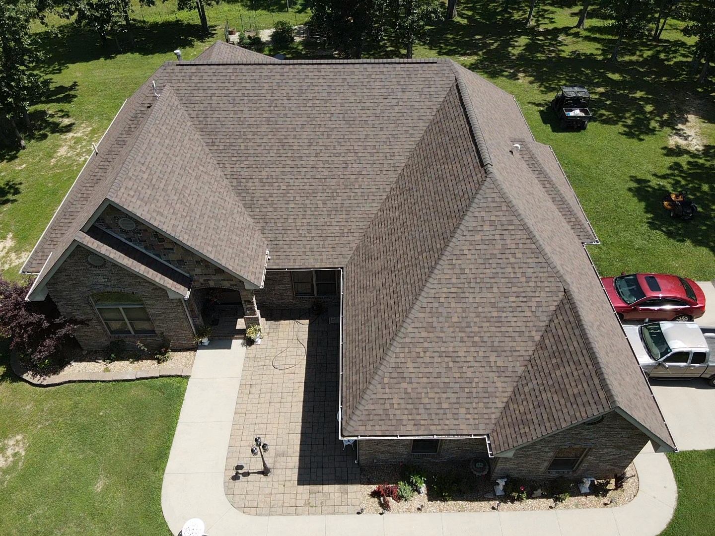 Aerial view of a brown-roofed brick house with a paved walkway, a car, and green grass.