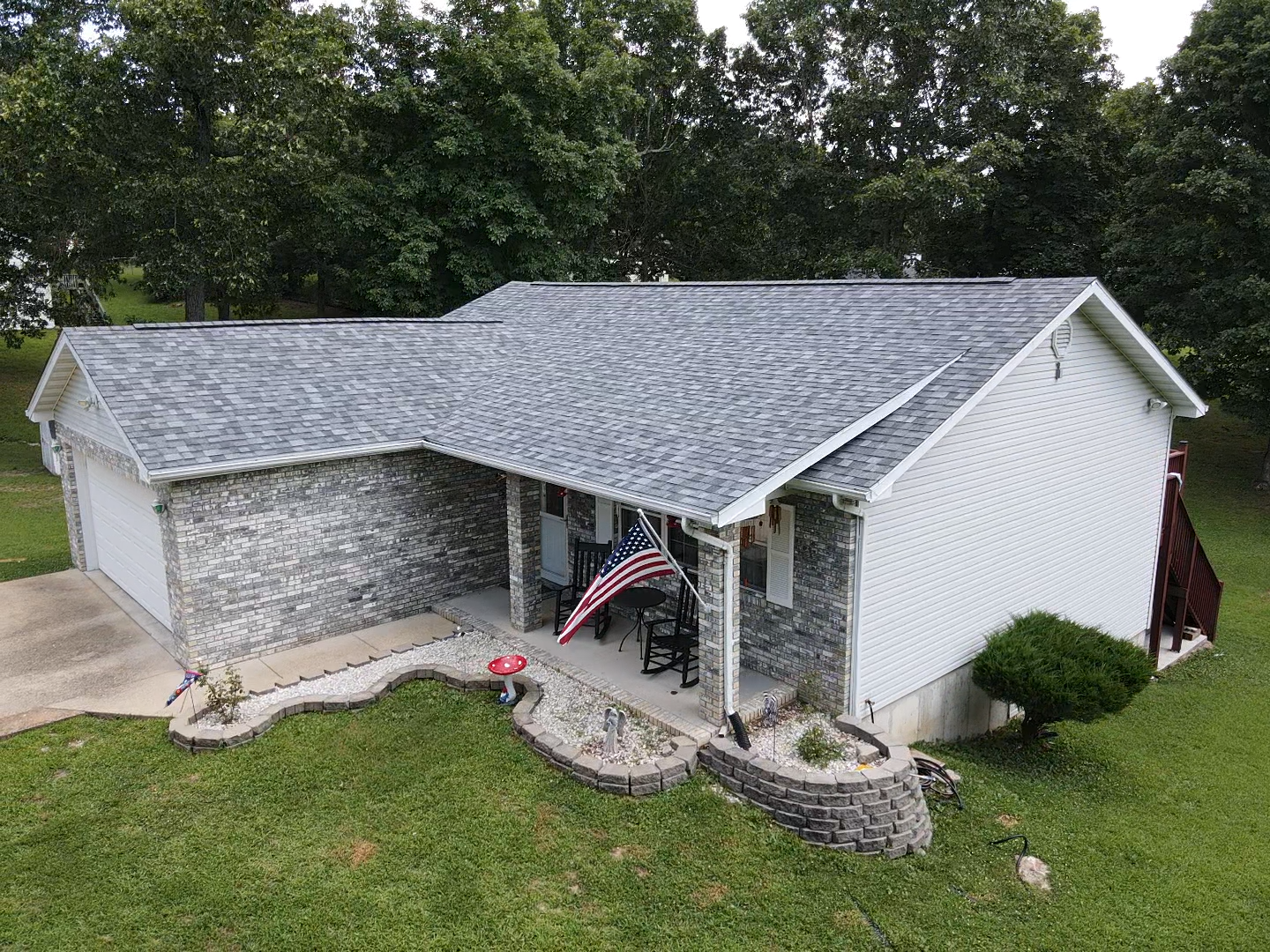 House with gray shingle roof, white siding, and stone facade. American flag hangs on the front porch.