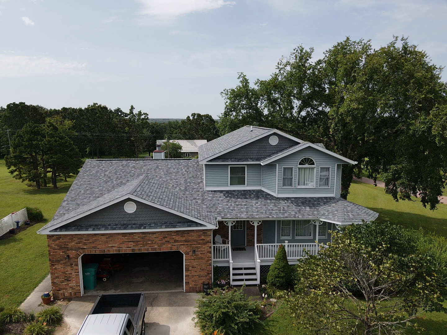 Blue and brick house with gray roof, porch, and attached garage in a grassy yard.