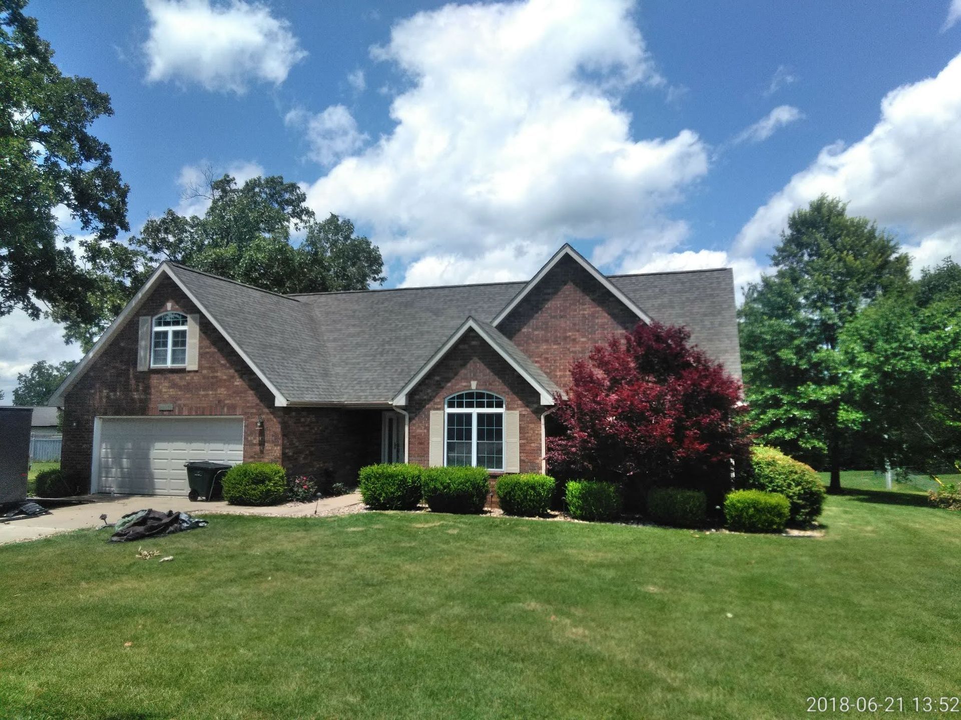Brick house with gray roof, green lawn, trees, and blue sky with clouds.
