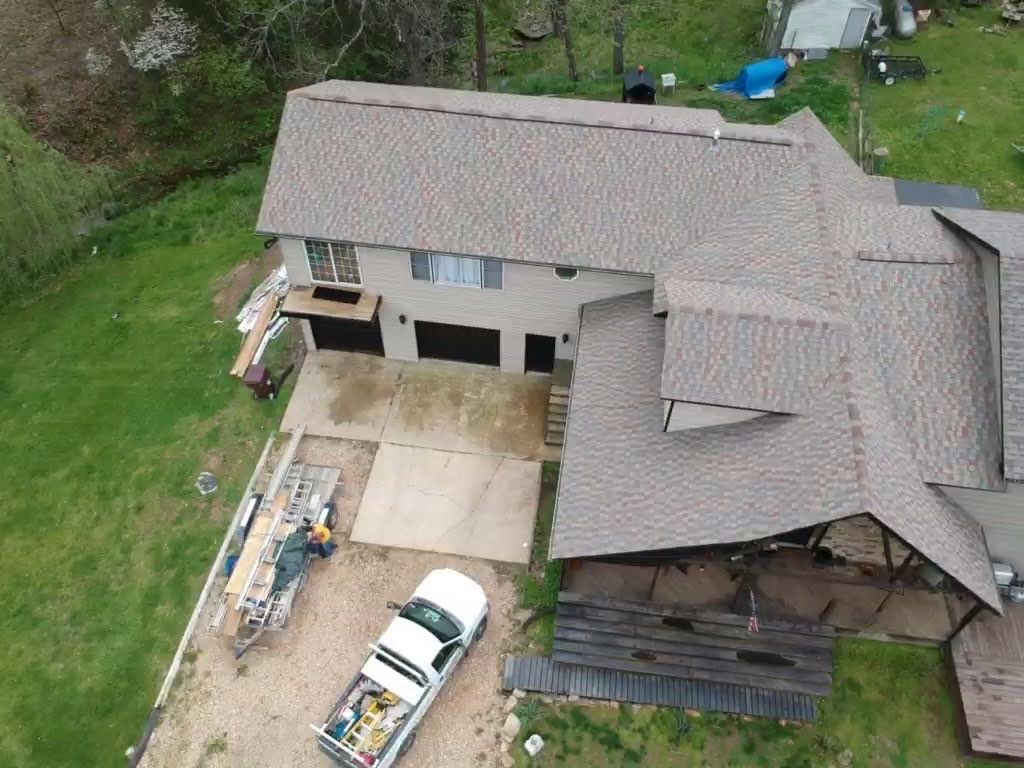 Aerial view of a house with a brown roof, gray siding, and a white truck parked in the driveway.
