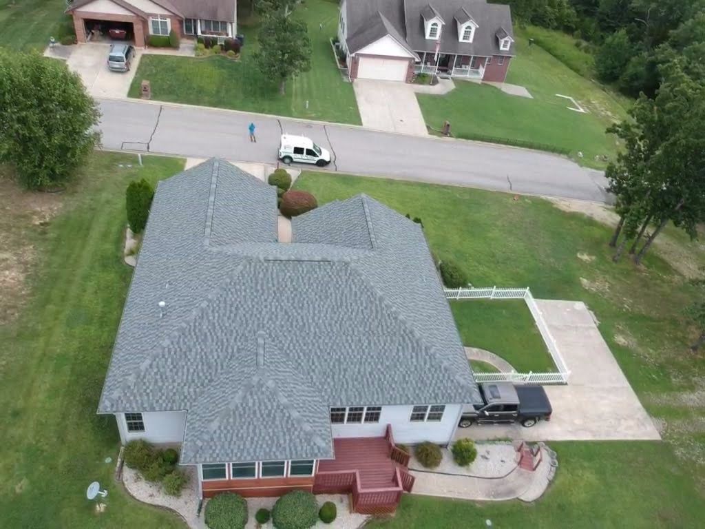 Aerial view of a gray-roofed house with a truck parked in the driveway; a van and person are seen on the street.