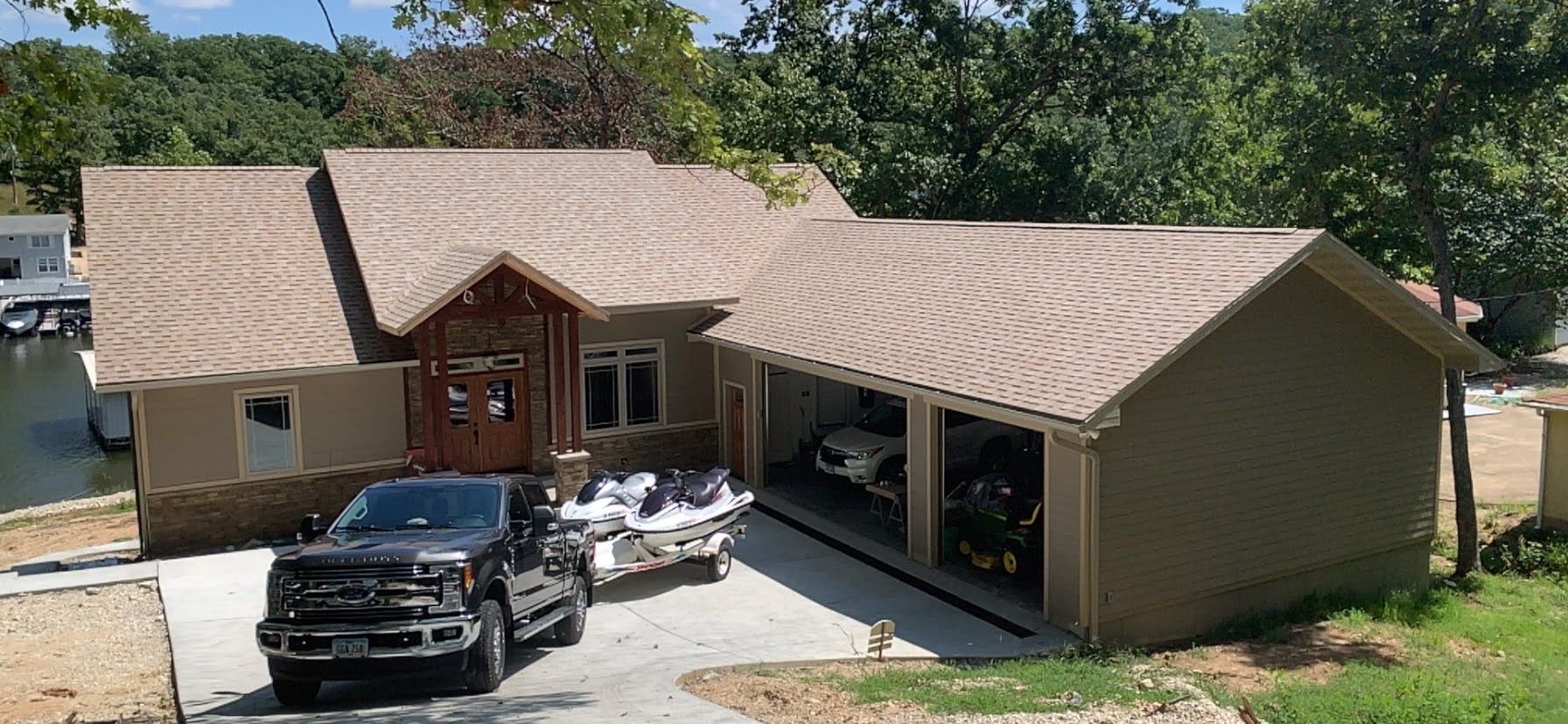 House with a garage, truck, and trailer with jet skis parked in the driveway. Trees in the background.