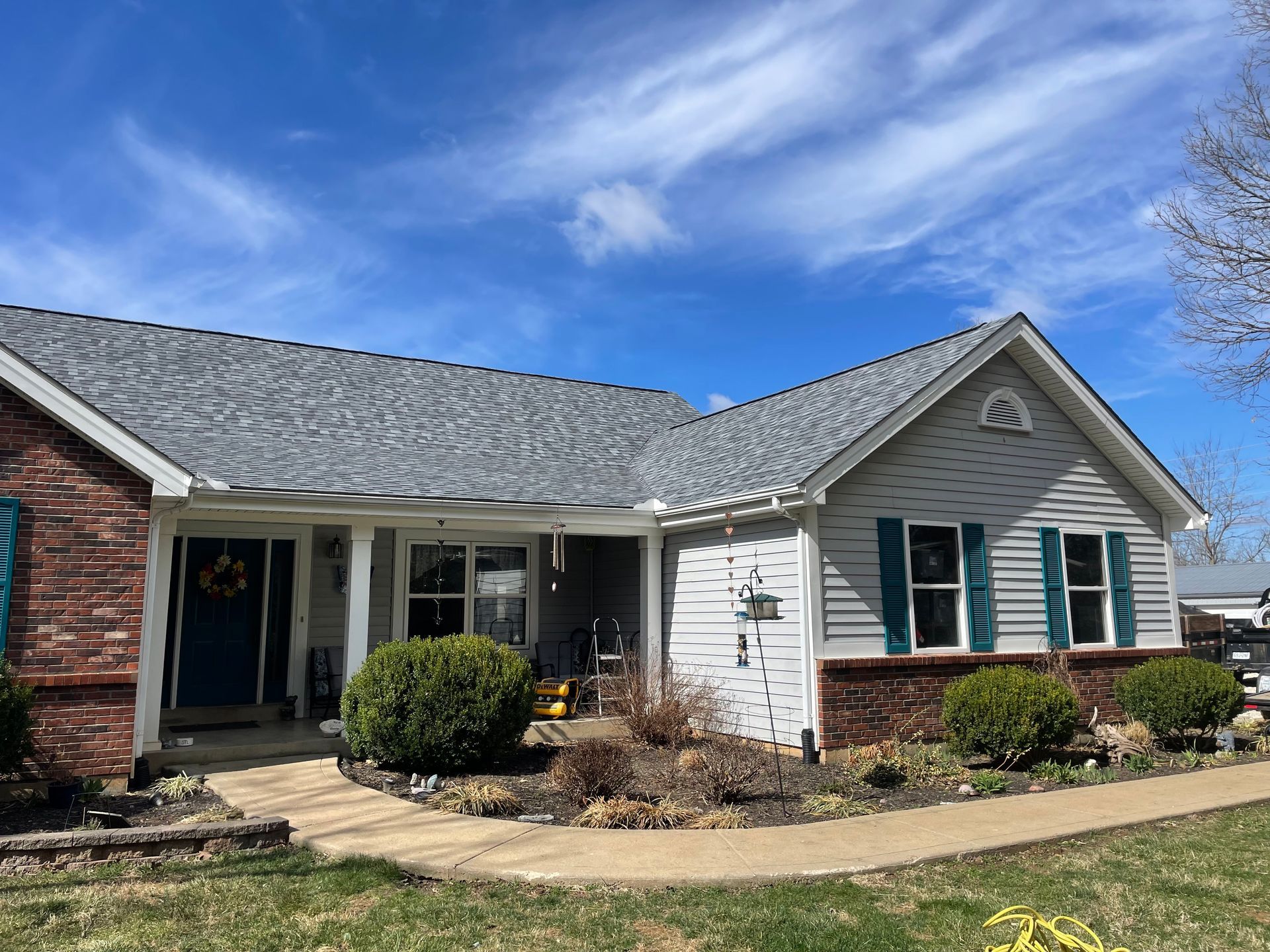 A residential house with gray roof and siding, blue shutters, and red brick facade under a blue sky.