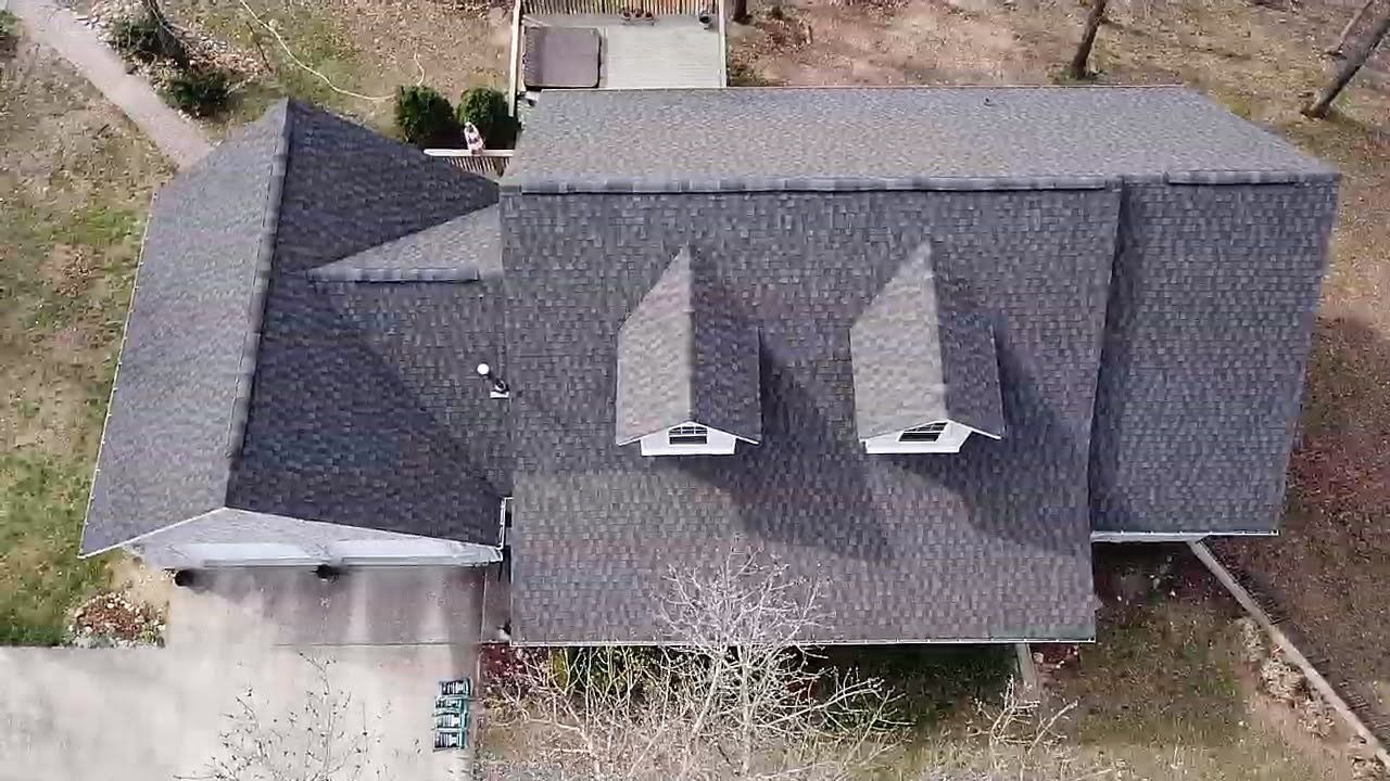 Overhead view of a house with a gray shingle roof, two dormers, and a driveway in front.
