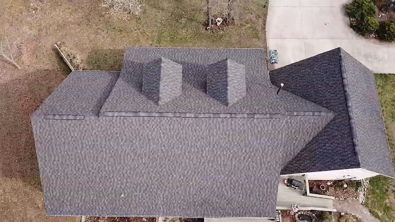Overhead view of a house with dark gray asphalt shingle roof, two dormers, and driveway.