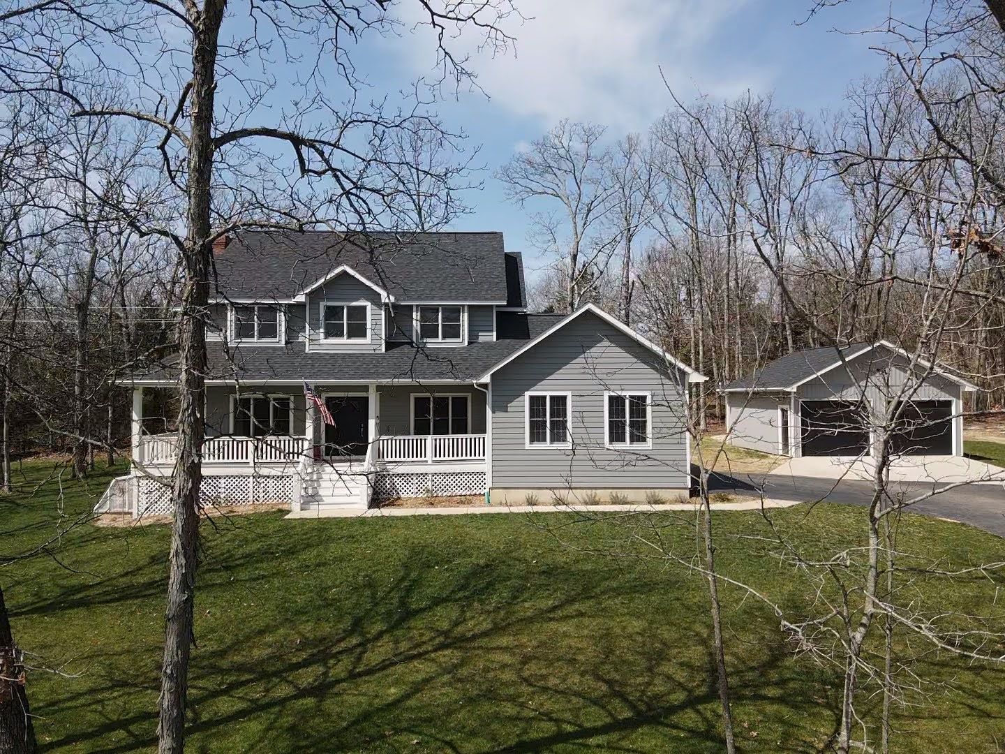 Gray two-story house with a porch and detached garage surrounded by trees.