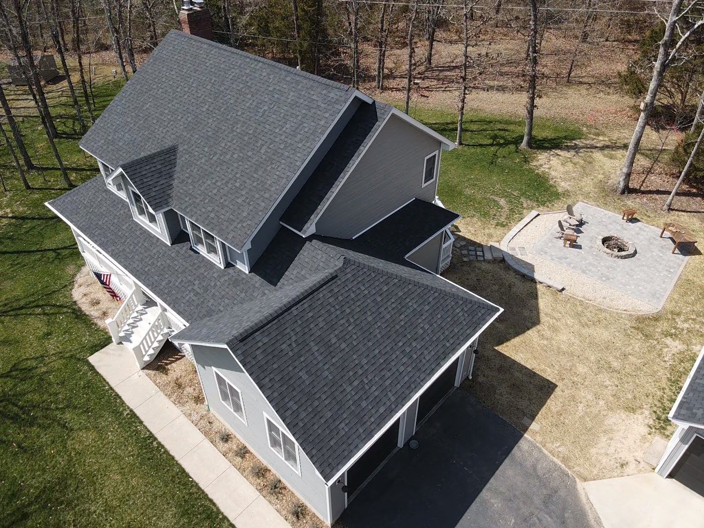 Aerial view of a gray house with a dark gray roof, surrounded by green grass and trees.