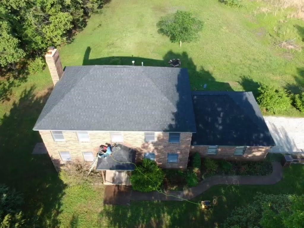 Aerial view of a two-story brick house with a dark gray roof, chimney, and surrounding green lawn.