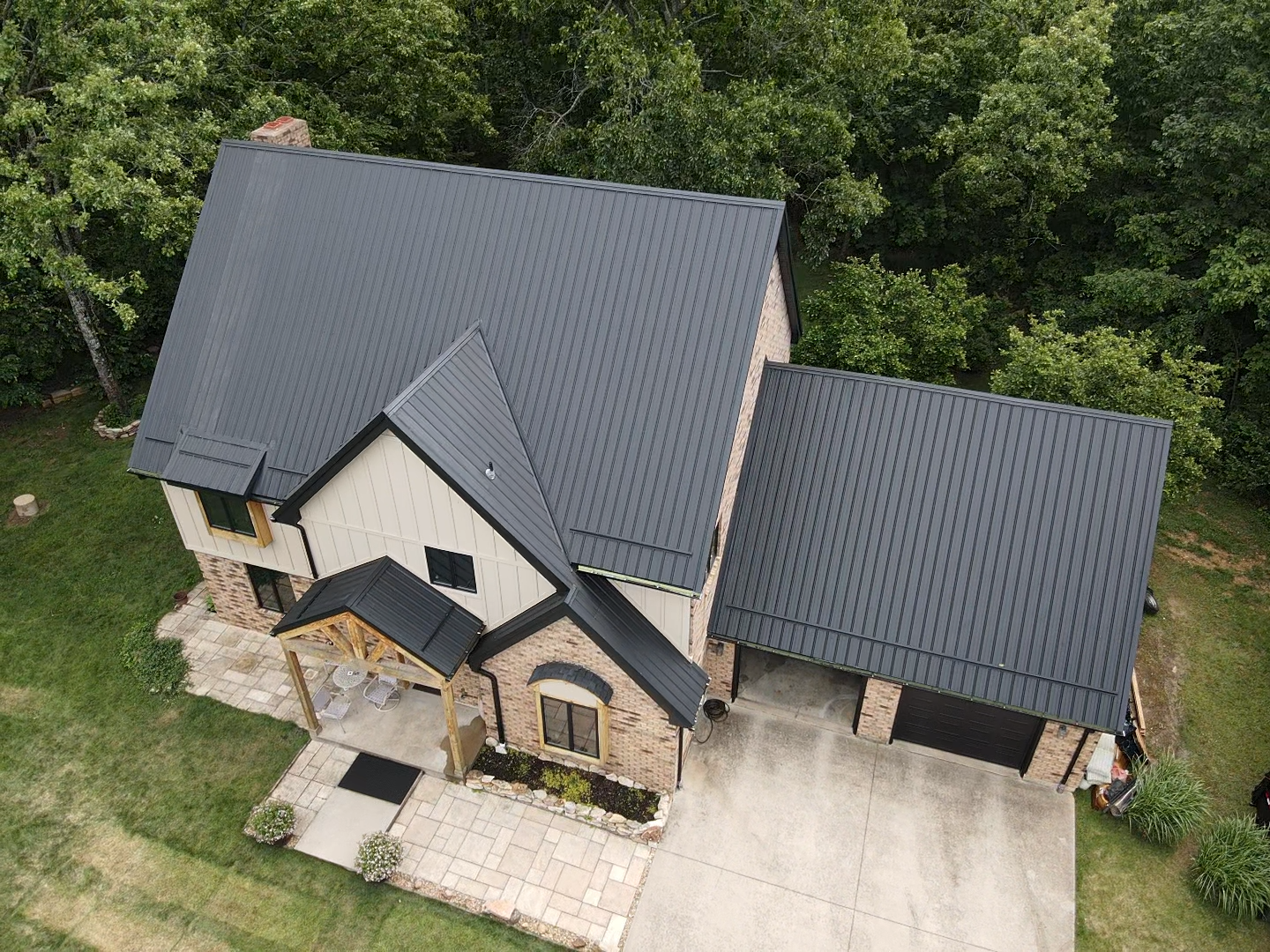 Drone shot of a two-story house with a black roof and garage, surrounded by trees.