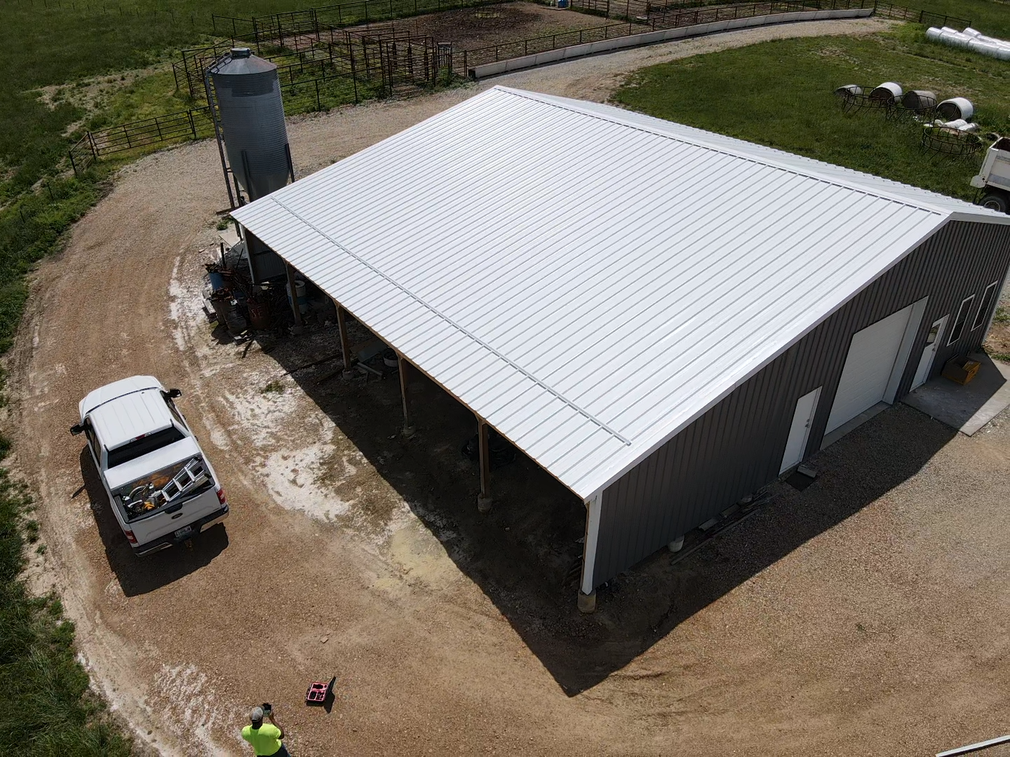 Aerial view of a gray farm building with a white roof and a pickup truck parked beside it.