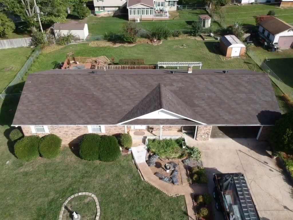 Overhead view of a brick home with brown roof, green yard, and a black vehicle in the driveway.