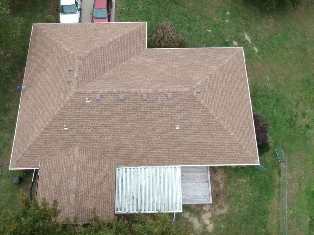 Overhead view of a house with a brown shingled roof, a white porch, and cars in the driveway.