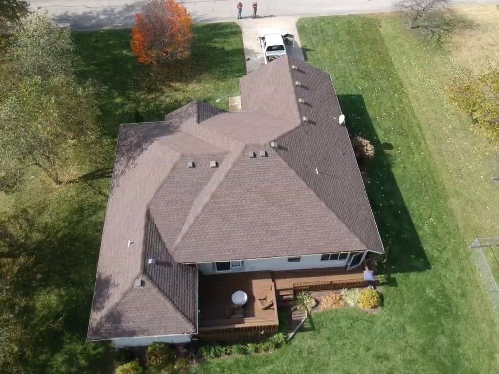 Overhead view of a house with a brown roof and wooden deck surrounded by green grass.