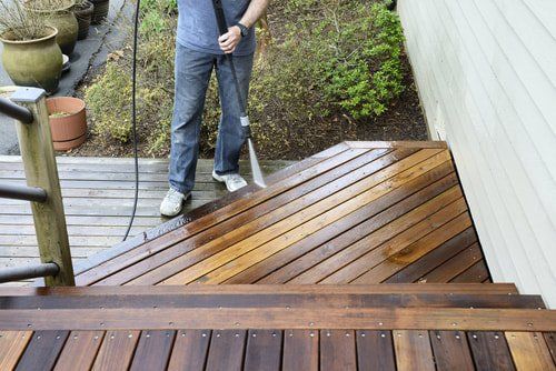 A Columbus Fence Professional powerwashing a deck and a deck installer staining a deck with a light colored deck stain
