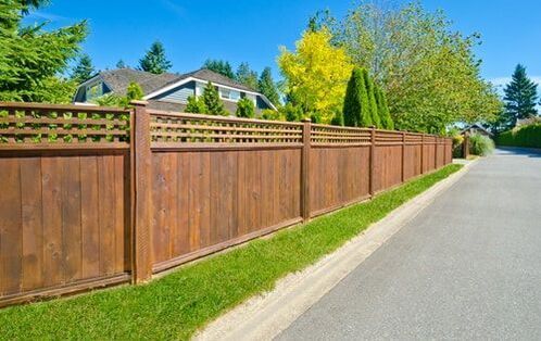A cedar stained wood semi-private fence with Lattice top and a short white vinyl fence rounding a corner in a neighborhood.