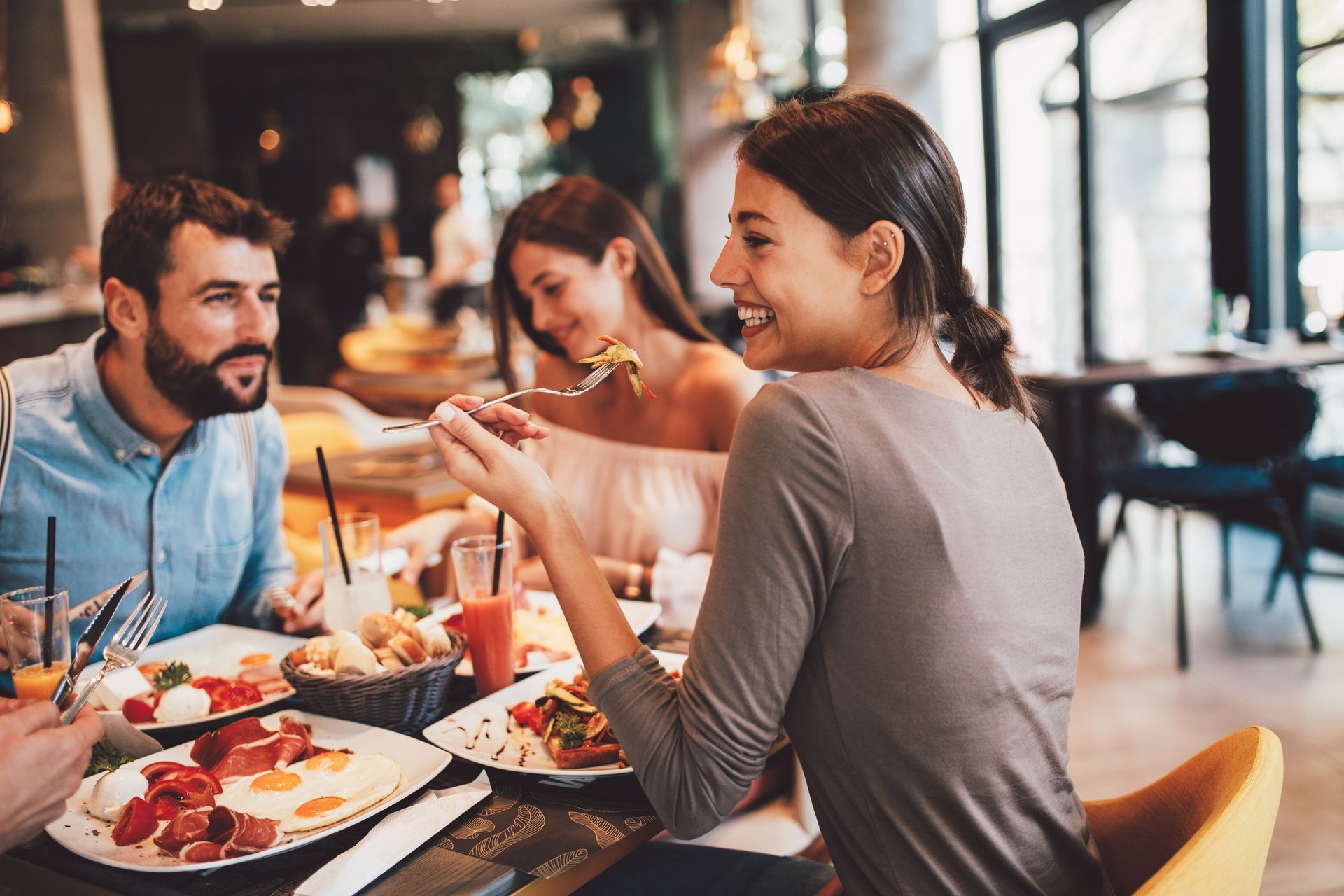 Three people eating a meal and smiling at each other in a brightly lit, modern restaurant.