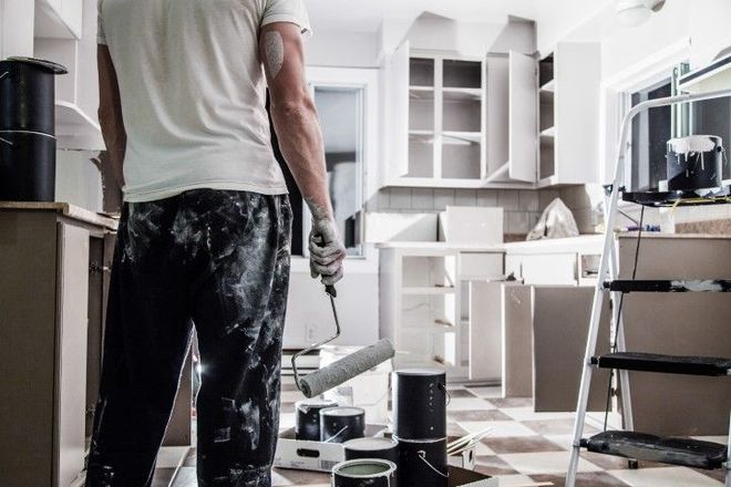 A man is painting a kitchen with a paint roller.