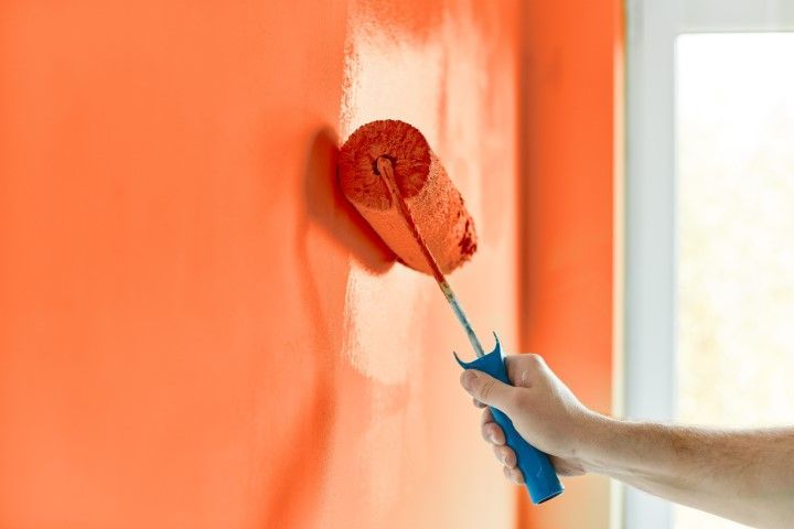 A person is painting a red wall with a paint roller.
