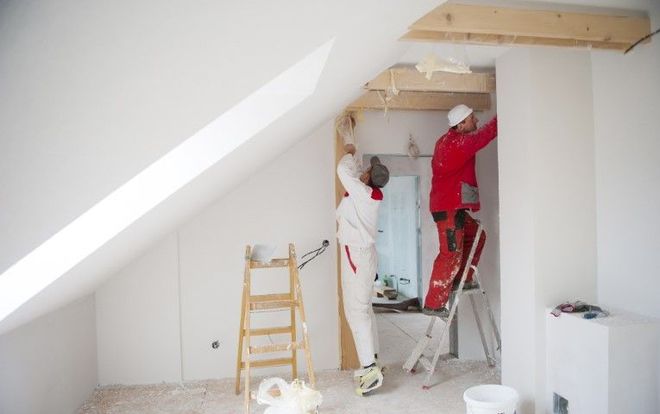 Two men are painting a room in an attic.