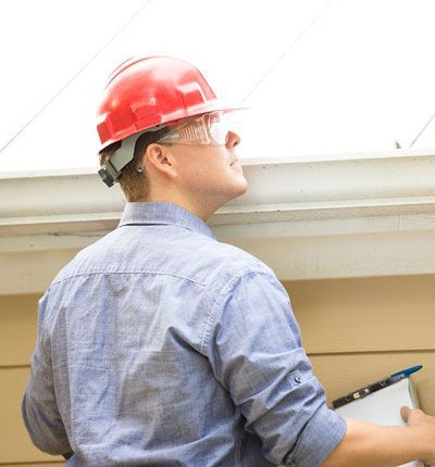 a man wearing a hard hat and safety glasses performing an eaves trough inspection