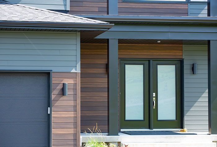 a modern house with a beautiful vinyl siding, a green door and a black garage door