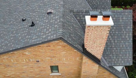 an aerial view of a brick house with an asphalt shingle roof and chimneys