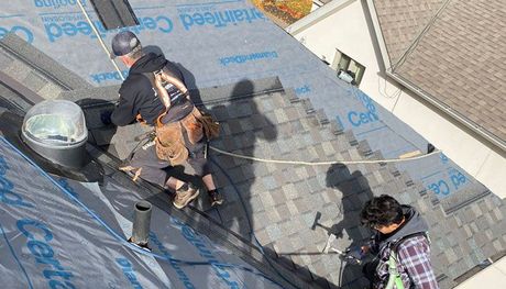 a group of experts working on the asphalt shingle roof of a house