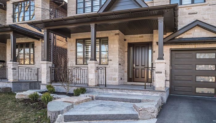 the front porch of a brick house with a brown door and steps leading up to it