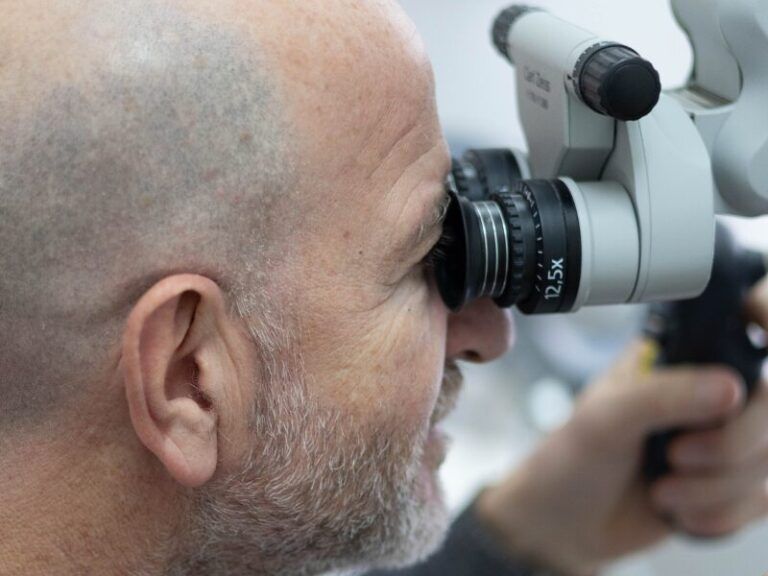 Uomo che osserva attraverso un microscopio dentale in una clinica, vista laterale ravvicinata.