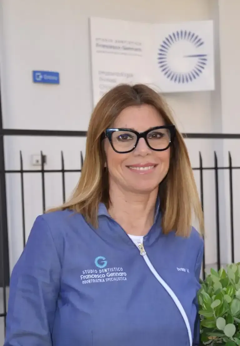Una donna in uniforme blu con gli occhiali sorride nella reception di un ufficio.