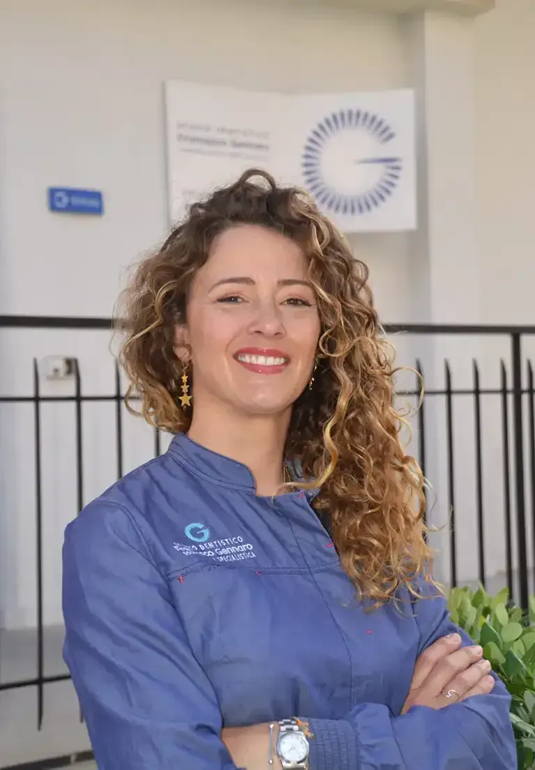Una donna sorridente in uniforme blu è in piedi con le braccia incrociate davanti a un edificio.