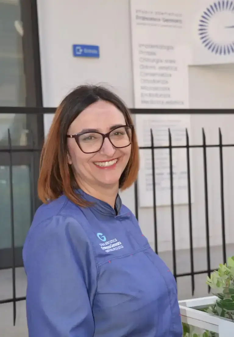 Una persona sorridente in uniforme blu è in piedi davanti a un edificio con una recinzione nera.
