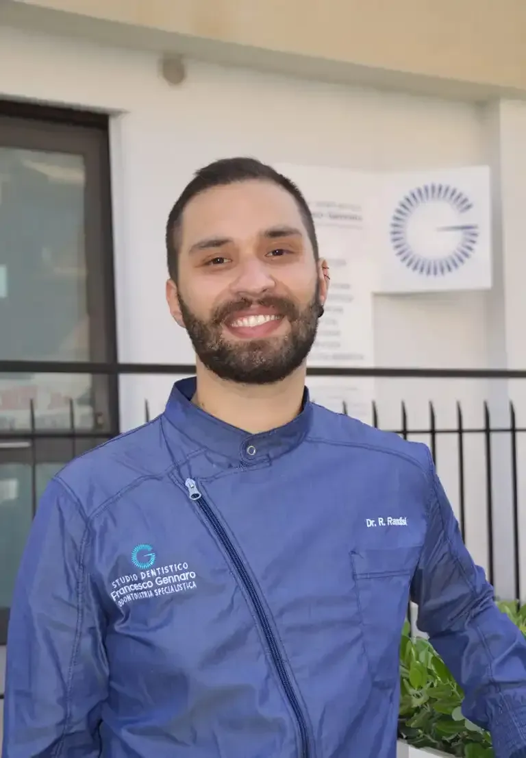 Persona sorridente in uniforme da lavoro blu in piedi davanti a un edificio.