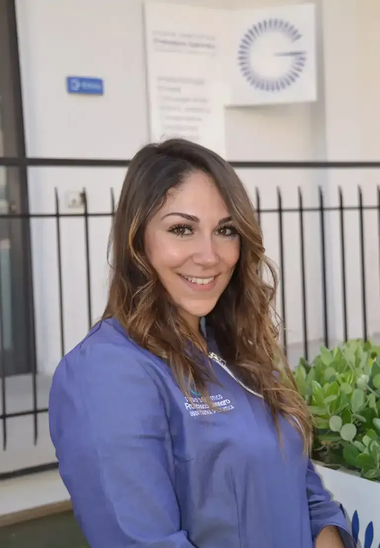 Donna sorridente con una camicetta blu in piedi all'aperto vicino a un edificio e a delle piante in vaso.
