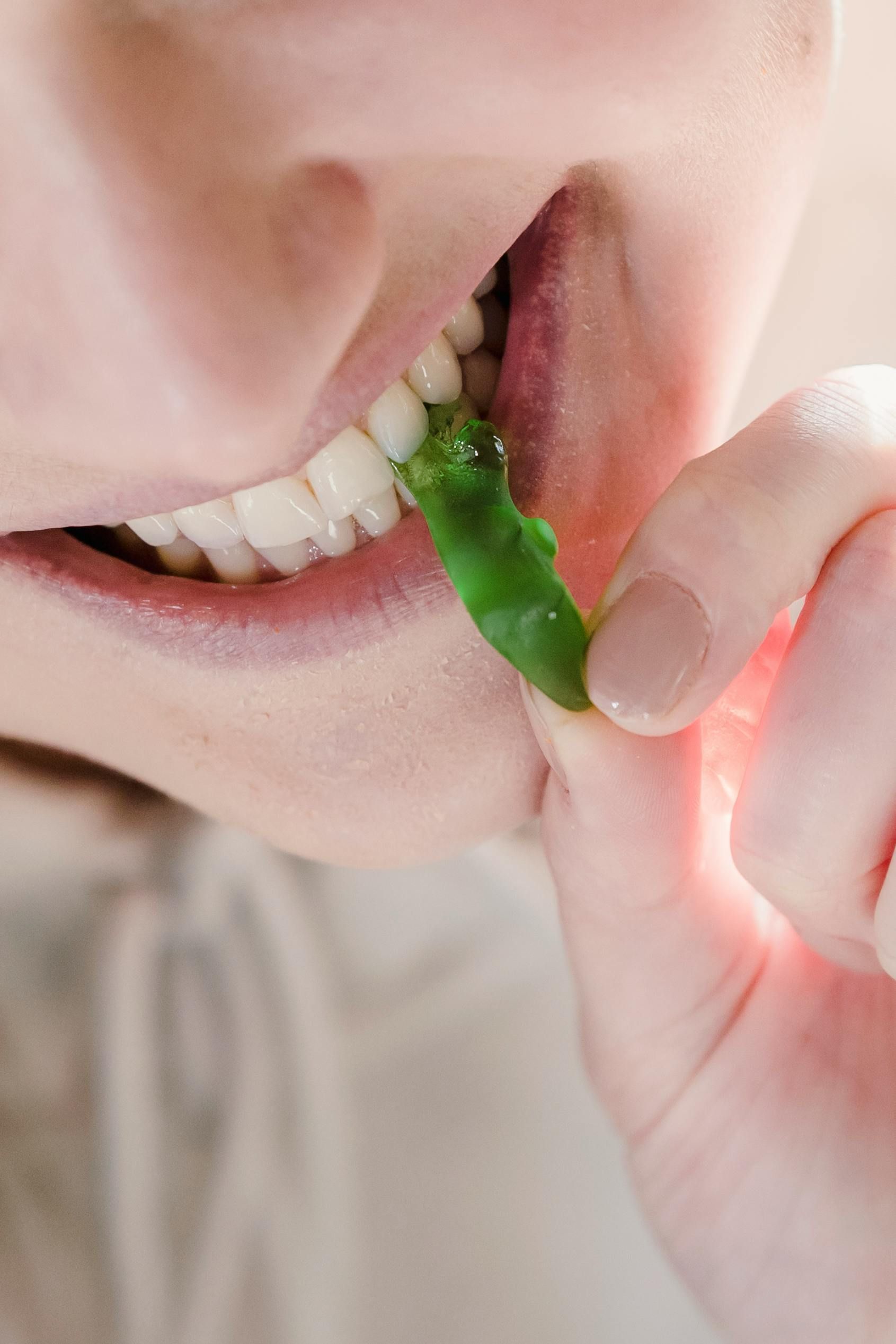 Primo piano di una persona che morde una caramella verde tenendola vicino alla bocca.