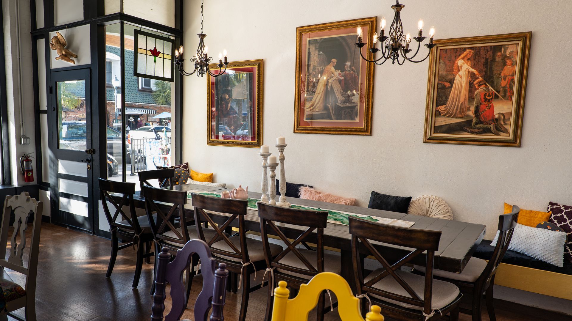 A dining room with a long table and chairs and paintings on the wall.