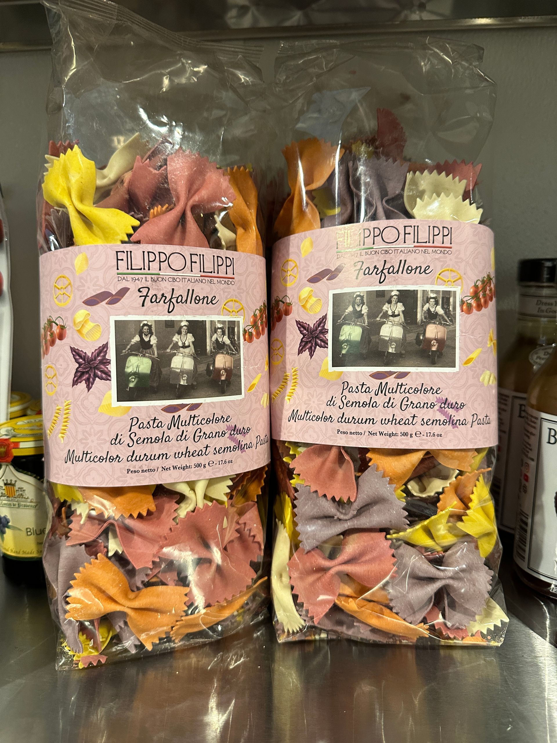 Two bags of colorful bow tie pasta are sitting on a shelf.