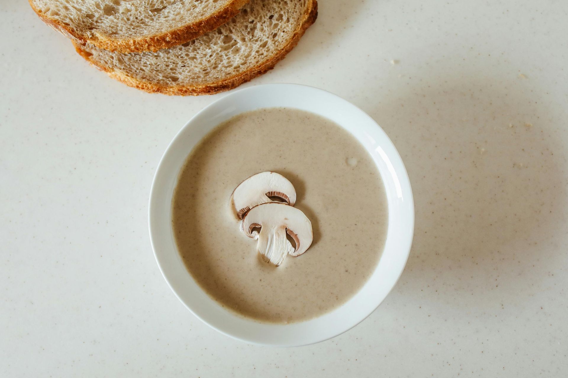 A bowl of mushroom soup with slices of bread next to it.