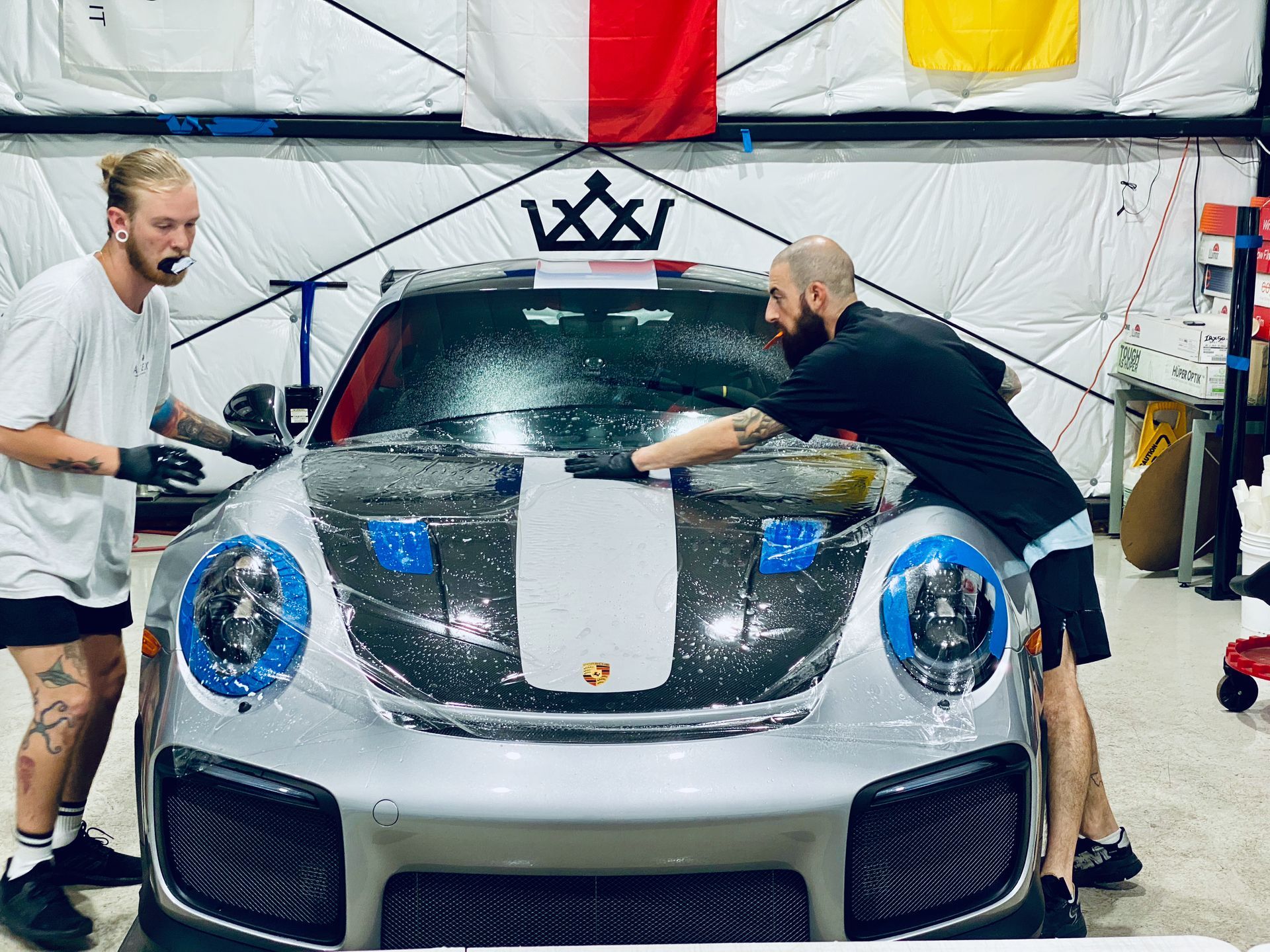 Two men are working on a silver sports car in a garage.